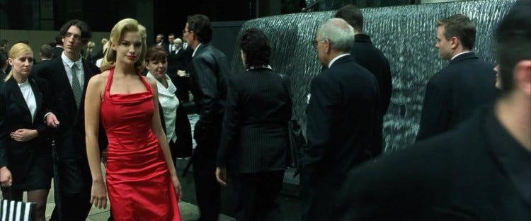 A woman in a red dress walks through a crowd of people in dark suits, from The Matrix.